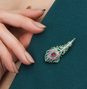 Detailed close-up of a luxury silver feather brooch with green and red zircon stones