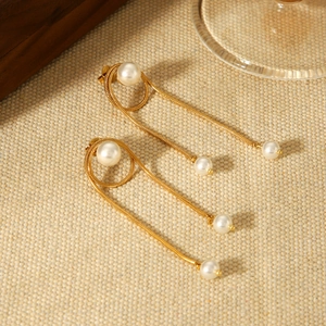 Close-up of gold snake chain tassel earrings with white pearls on a textured fabric