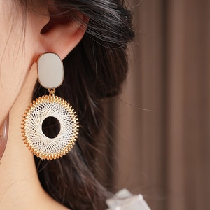 Close-up of bohemian gold hoop earrings with white woven mesh pattern on a female model