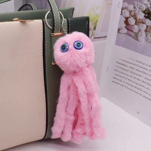 Detail view of pink plush octopus keychain hanging on a stylish green handbag