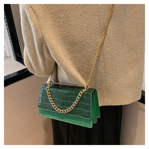 Détail d'un sac à bandoulière vert effet crocodile avec chaîne dorée sur mannequin