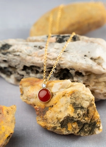 Macro detail of gold necklace with red round gemstone on a natural textured stone