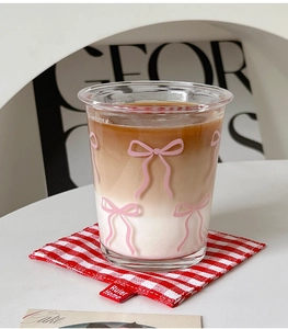 Detail of clear glass cup with pink bow pattern on a red checkered coaster