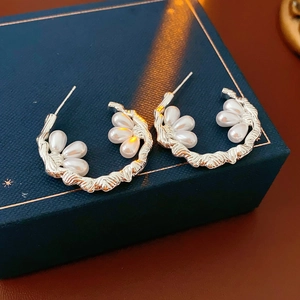 Macro view of C-shaped silver floral earrings with drop pearls on a blue jewelry box