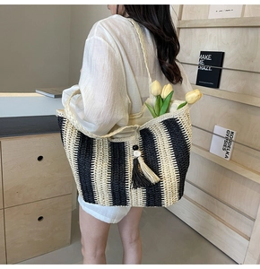 Detail of vertical black and white striped straw tote bag with decorative tassel accents