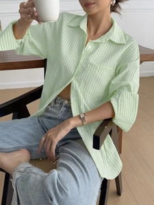 Women's casual green striped long sleeve shirt styled with jeans in a home setting