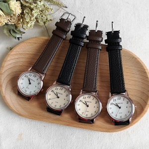 Classic quartz watches with round dials and leather straps on a wooden tray