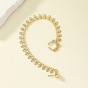 Detail of gold heart chain earring with ear cuff displayed on textured beige background