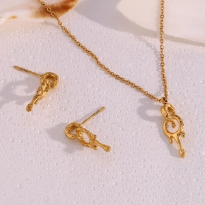 Macro detail of 18K gold plated lava-style necklace and earrings set on a textured surface