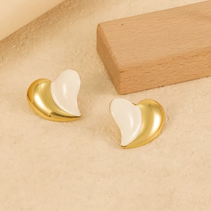 Macro shot of two-tone gold and white heart earrings on a minimalist textured background