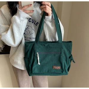 Detailed view of green corduroy tote bag with zipper pocket held by model in casual style