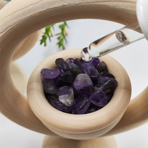 Close-up of essential oil being dropped onto raw amethyst crystals in a wooden bowl