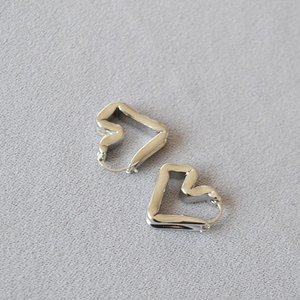 Detail of silver abstract heart earrings with polished finish on gray textured fabric