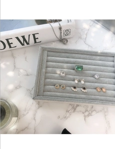 Détail du plateau à bijoux en velours gris avec bagues et boucles sur fond de marbre
