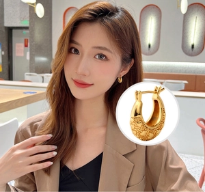 Detail of 18K gold U-shaped hoop earrings with embossed heart pattern on a model