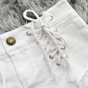 Dettaglio di pantaloncini di jeans bianchi elasticizzati con lacci e bottoni d'oro