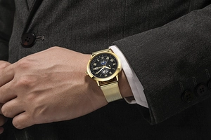 Golden business watch with mesh strap shown under a formal suit sleeve for men