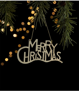Golden Merry Christmas metal lettering ornament hanging on a pine tree branch
