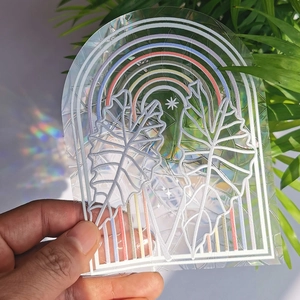 Close-up of holographic rainbow suncatcher sticker with tropical leaf and prism effect