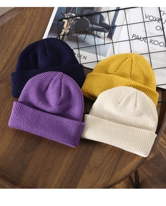 Flat lay of ribbed knit beanies in navy, purple, yellow, and beige on a wooden table