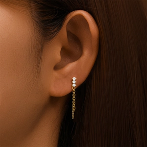 Gros plan d'une boucle d'oreille en argent S925 doré avec trois zircons et pompons en chaîne