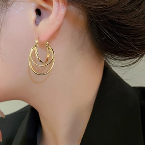 Detailed view of triple-layered golden metal hoop earrings on model with elegant glow