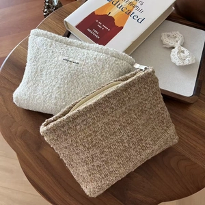 Flat lay of tweed cosmetic bags in beige and light brown with a gold zipper on a wooden desk