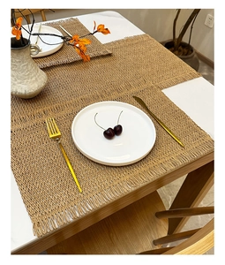 Close-up of woven table mats with fringe on a wooden table with elegant tableware