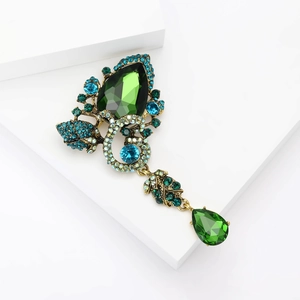 Detail of vintage teardrop green gemstone and blue crystal brooch with bronze plating