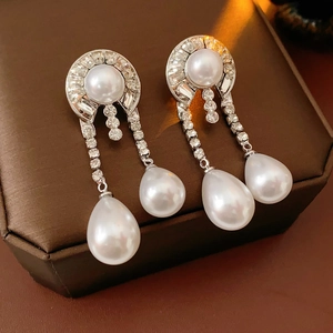 Dettaglio macro di orecchini pendenti vintage con strass scintillanti e perle bianche