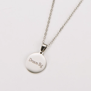 Detailed close-up of a silver metal necklace featuring a Dream Big engraved circular pendant