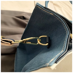 Detail of blue denim tote bag featuring golden metal swivel hook and contrast stitching