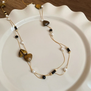 Detail of vintage necklace with heart tiger eye stone and pearls on ceramic plate