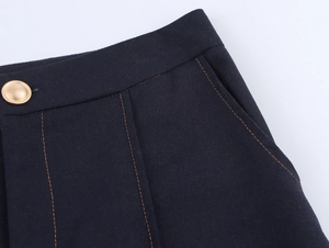 Detailed view of dark woven fabric waist with golden button and orange contrast stitching