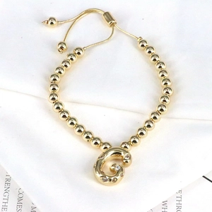 Detail of gold beaded bracelet with zircon-studded letter G charm on white paper
