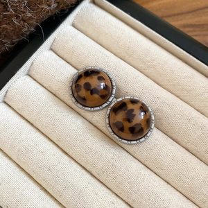 Macro detail of leopard print leather stud earrings with silver-tone beaded metal edges