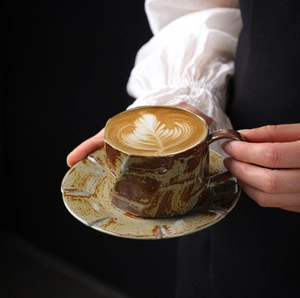 Close-up of handmade ceramic coffee cup with mottled glaze held by hands