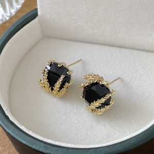 Macro shot of gold wheat-ear square earrings with black gemstone in a jewelry box
