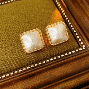 Close-up of gold square earrings with white textured beads on a vintage wooden frame