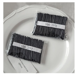 Detail of 100 black metal wavy bobby pins in transparent packaging on a white ceramic tray