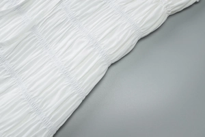 Détail du tissu blanc texturé montrant le travail du smock et les plis élastiques