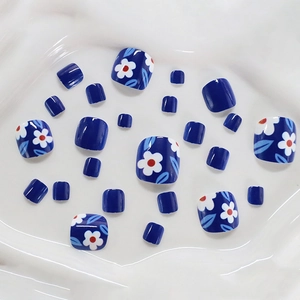 Short square blue press-on toenails with white floral daisy patterns on white tray