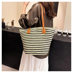 Close-up of a striped straw tote bag with brown leather handles in a cafe setting