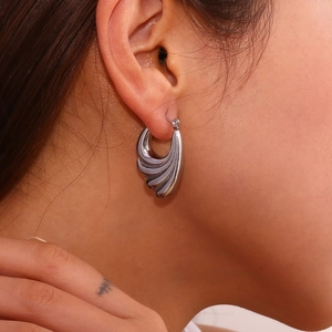 Macro shot of silver wave-shaped hoop earrings with a polished metallic finish on model
