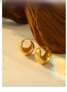 Macro shot of gold-plated chunky C-shaped hoop earrings with inner striped texture detail