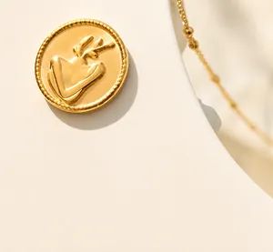 Close-up of a gold-plated coin necklace featuring an embossed elk motif on a white stand
