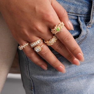 Close-up of five luxury gold rings with zircon and green gemstone on hand