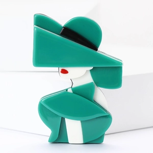 Detailed close-up of acrylic lady brooch with green hat on white geometric blocks