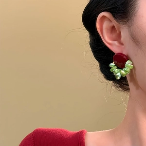 Close-up of red and green geometric earrings on a model wearing a red knit top