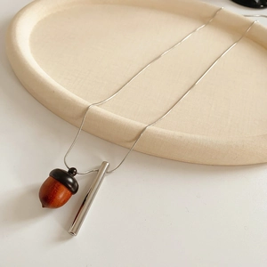Detailed view of wood acorn and silver metal bar pendant on an oval beige plate